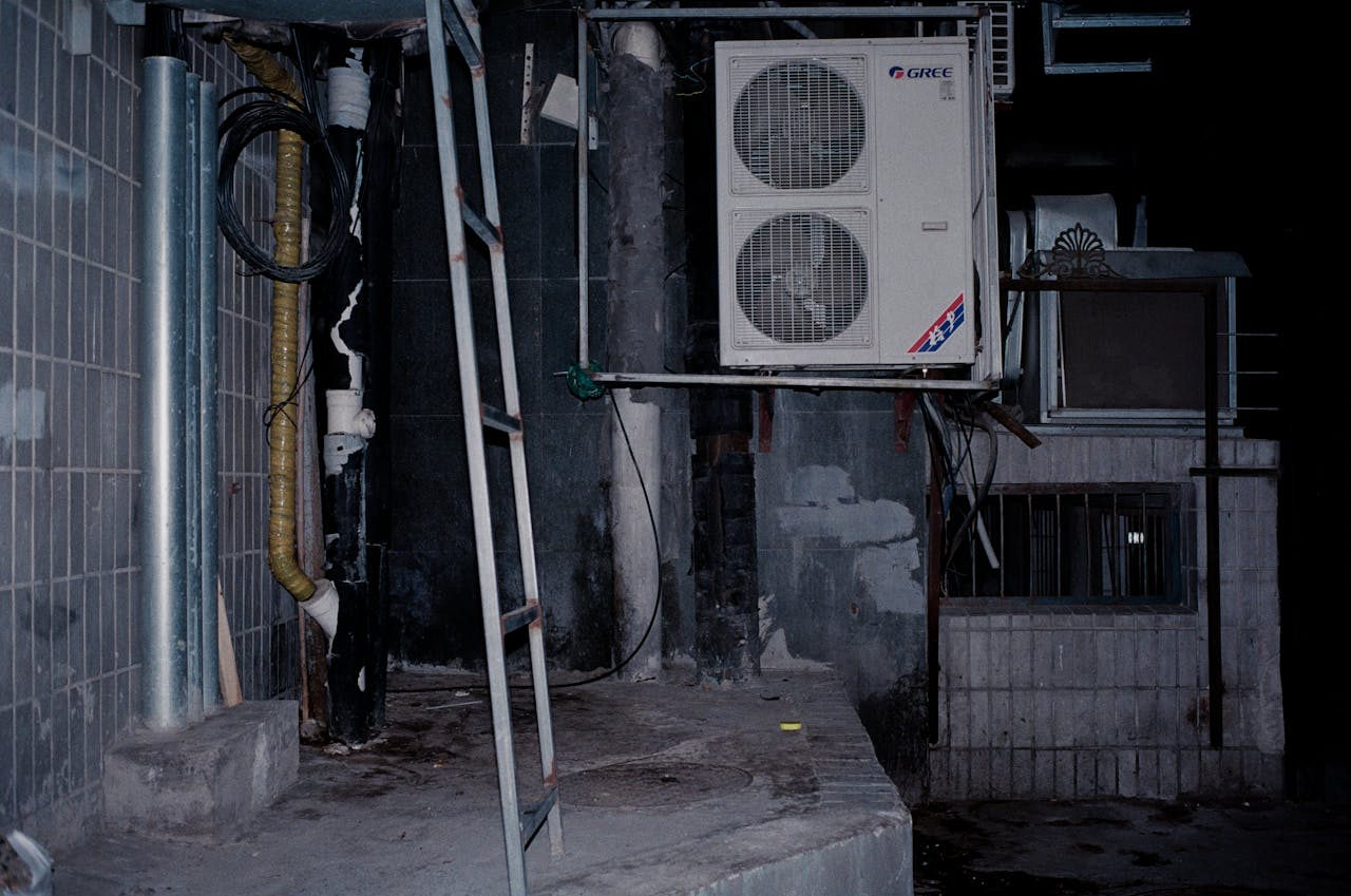services-04 Close-up of an industrial air conditioner setup on a building wall, showcasing pipes and a ladder.