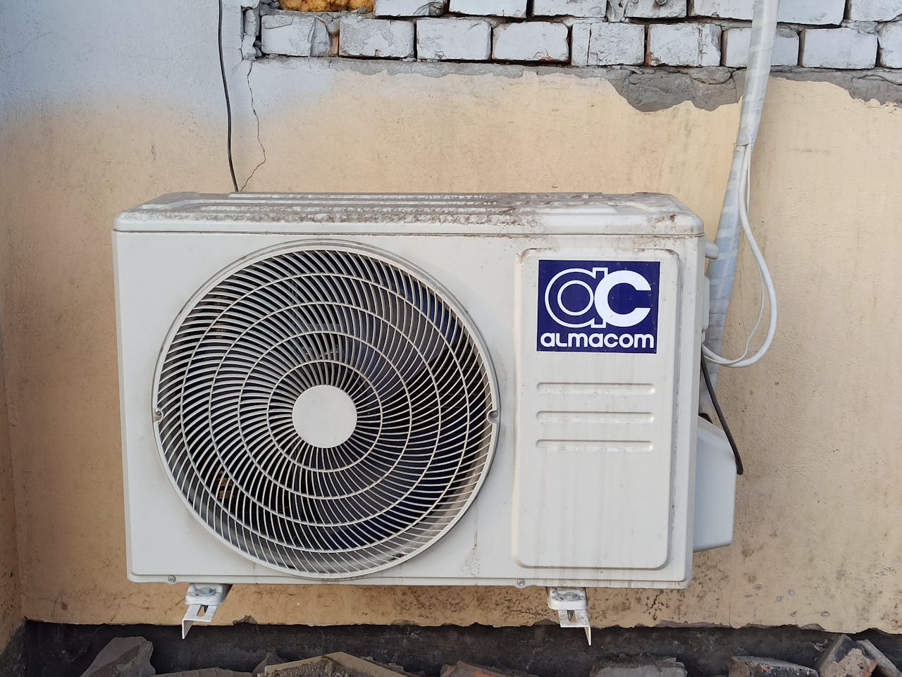 services-02 A well-used outdoor air conditioning unit affixed to a brick wall, showcasing urban climate control.