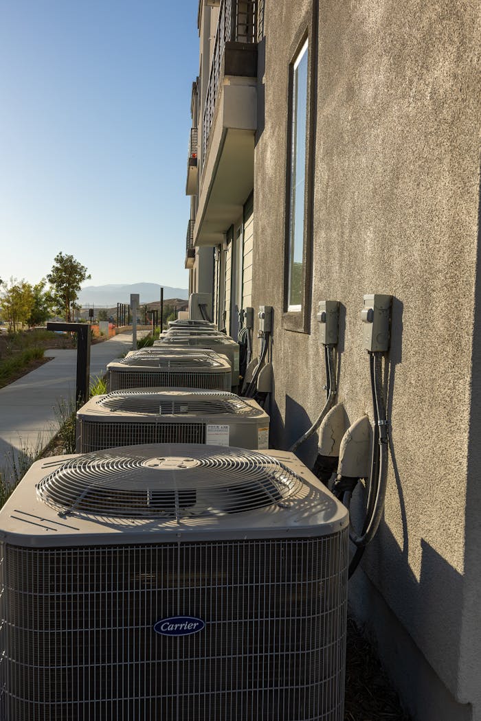 why-choose-us Line of air conditioning units on a city apartment exterior with a sidewalk view.