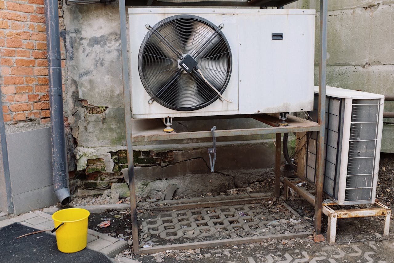 who-we-are Exterior view of an industrial air conditioning unit with visible wear and rust, set against a shabby wall.