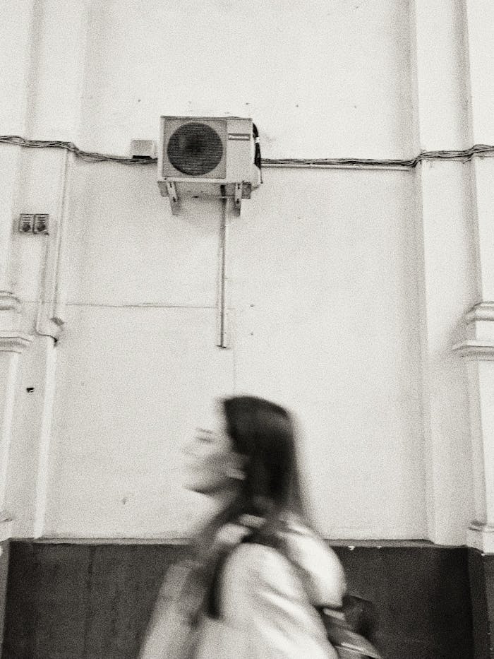 services-04 Black and white side view of young female walking near shabby wall of building with air conditioning